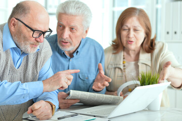 senior people sitting at table, working with laptop