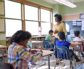 School, children and teacher in a classroom while talking to kids to study and learn knowledge and...