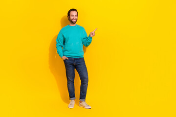 Fototapeta premium Full length photo of cool excited man wear turquoise clothes pointing finger empty space isolated yellow color background