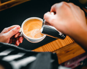 Close-up of the hand of a professional barista in a coffee shop making  pouring steamed milk into the coffee cup making latte menu
