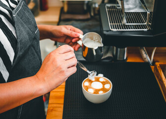 Hand of a barista in the coffee shop preparing to steam milk in the jug for a coffee cappuccino menu.
