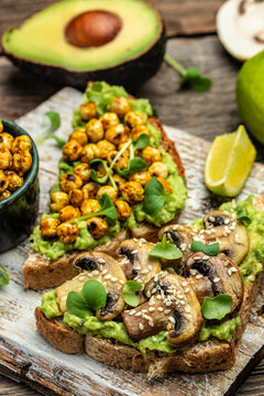 Healthy avocado toasts with chickpeas and mushrooms on a wooden background, vegetarian vegan food. vertical image. top view. place for text