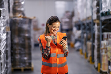 A warehouse worker celebrates success and smiling at the camera.