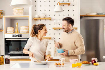 A happy couple is preparing eggs for breakfast in the morning at home.