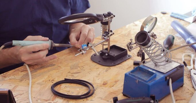 Electronics serviceman applying tin at micro switch contacts using soldering iron, close up