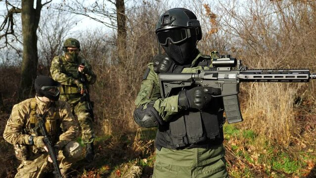 A special forces squad in military uniform with weapons in the forest. Soldiers in camouflage and machine guns in balaclavas, glasses and gloves. The concept of war and combat operations.