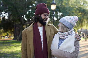 Happy caucasian couple outdoors looking at each other and laughing during their walk around a park.