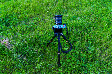 A modern mirrorless camera is mounted on a tripod against the background of a green lawn. Professional photographer while working.