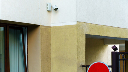 A video surveillance camera is installed at the entrance to the parking lot. Paid guarded car Parking. Closed gates and a road sign prohibit entry. CCTV camera on the wall.