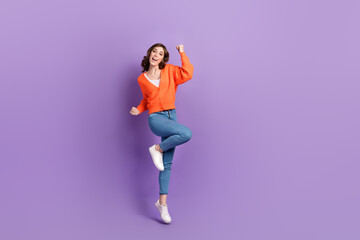 Fototapeta na wymiar Full length photo of lucky cheerful lady wear orange cardigan jumping high rising fists empty space isolated violet color background
