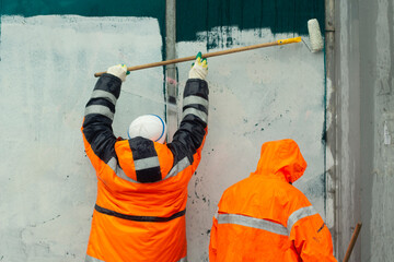 Fototapeta premium Workers paint wall. Wall flogging. Orange clothing of workers. Smearing graffiti.