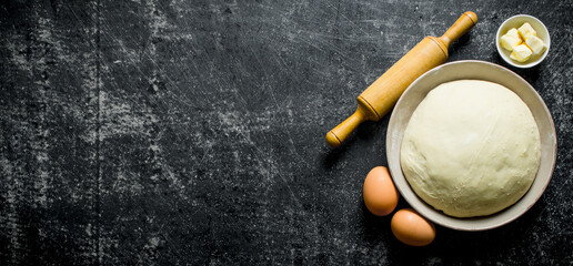 Dough in bowl with eggs, rolling pin and butter.