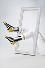 Cropped shot of slim woman's legs bent. The sexy girl is wearing white jeans and a colored striped socks with a wide rubber band. The attractive lady is posing in a frame on the light background.