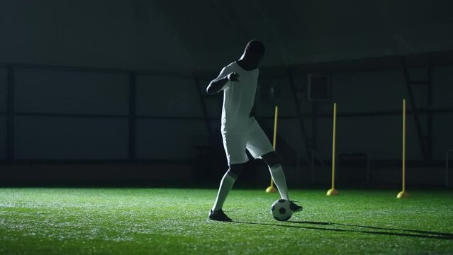 full-length shot of training football player in sport hall, black sportsman in uniform kicking ball