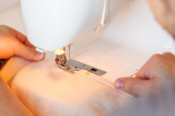 Young mans hands feeding canvas fabric through sewing machine