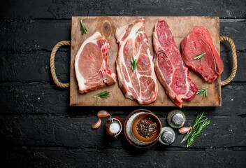 Raw meat. Pork and beef steaks on a tray with spices and rosemary sprig.