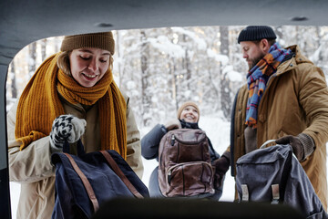 Family taking the bags out of the car, they arranging winter holiday in nature
