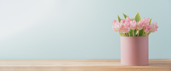 Bouquet of fresh pink tulips in gift box stands on  wooden table on turquoise background. Gift for...