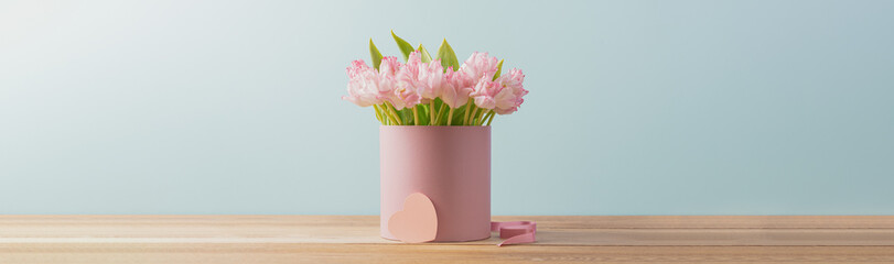 Bouquet of fresh pink tulips in gift box stands on  wooden table on turquoise background. Gift for...