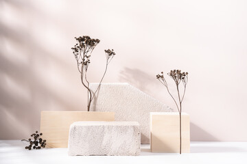 Concrete and wooden cube podiums with dry plants on light beige background. Minimal wooden stand for branding and packaging presentation