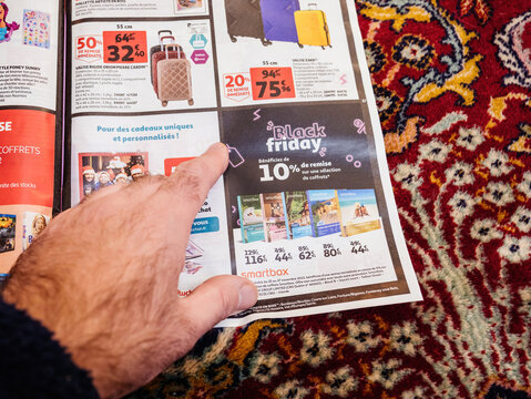 Paris, France - Dec 2, 2022: Man reading Advertising leaflets of Cora supermarket chain selling furniture, electronics home object special black friday prices for the smartbox gifts