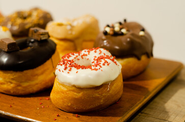Assortment of donuts with different flavors displayed on a table. Selective focus of a cream-filled donut with decorative strawberry pearls