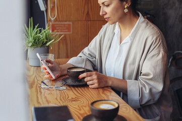 A young woman sitting in a cafe with a cup of coffee, looking at her smartphone