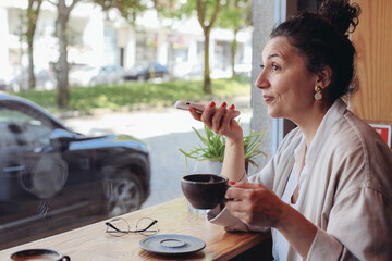 And young woman sitting in a cafe with a cup of coffee and recording an audio message 