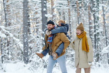 Happy family walking with child in the forest during winter day