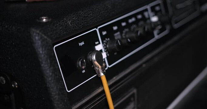Male hand Plugging in guitar cord cable into the input jack of amplifie