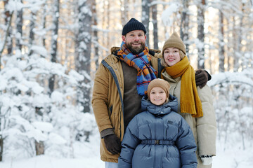 Portrait of happy family with their daughter smiling at camera together standing in winter forest