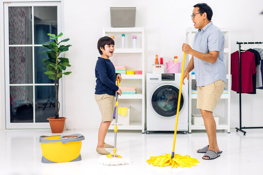 Father teaching asian kid little boy son having fun doing household chores cleaning and washing floor wiping dust with mopping while cleaning house together at home