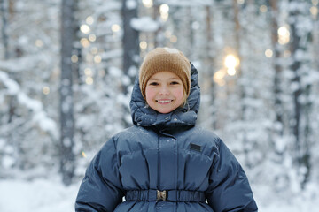 Portrait of little girl in warm clothing smiling at camera walking in winter forest