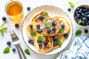 Healthy breakfast. Pancakes with fresh blueberries and honey at white table, served with mint leaves. Top view with copy space.