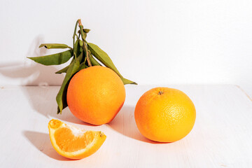 Fresh ripe oranges with leaves and orange slice on white table in sunlight. Healthy food concept, closeup