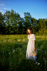 a beautiful woman in a light, light, summer dress is standing in a flowering meadow in the sunset light
