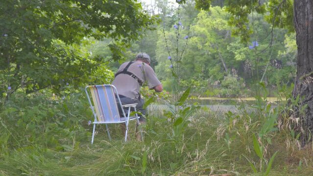 A man tourist sits in a chair in the forest on the banks of the river and drinks tea from a mug
