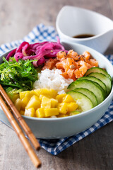 Poke bowl with rice, salmon,cucumber,mango,onion,wakame salad, poppy seeds ands sunflowers seeds on wooden background