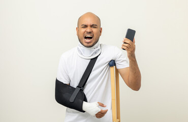Depressed upset man suffering from pain. Broken arm. Asian man put on plaster bandage cast splint with cellphone. Patient wearing sling support arm after accident injury. life insurance and accident