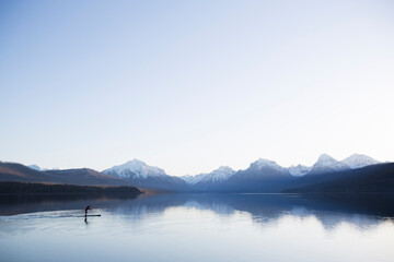 A man stand up paddle boards (SUP) on a calm Lake McDonald in Glacier National Park.