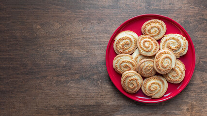 Sugar spiral biscuits on the red plate on the wooden table, banner. Homemade round cookies, top view. Pastry concept