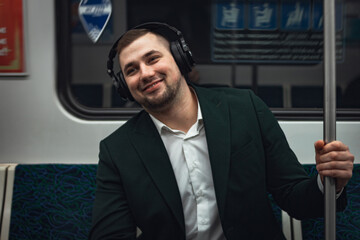 man young male caucasian passenger one person positively cheerful listens to music in headphones, smiles and go by subway transport in the morning. concept subscription to music.