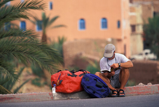 A  male traveler waiting for a ride in a foreign country.