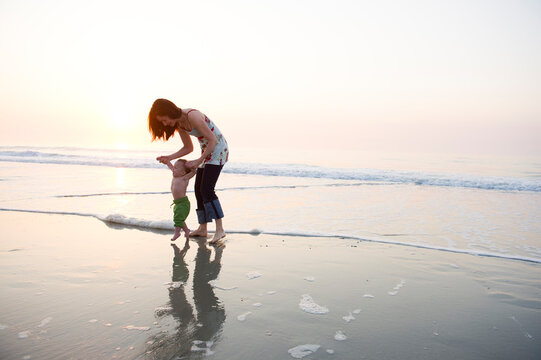 Water washes onto the beach as a mother helps her infant son take his first steps on the beach on Pawleys Island, South Carolina.