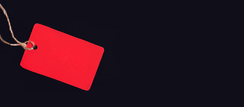 An empty red price tag with a place to insert text on a string on a black background. Copy space