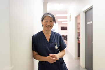 close up shot of a female middle aged healthcare worker leaning on the wall smiling at the camera