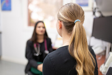 Close up shot of a woman's back head with a blonde hair in pony tail talking to a doctor in a clinic