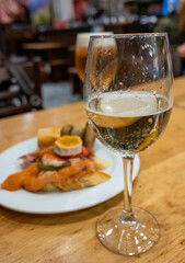 Board with typical snacks of Basque Country, pinchos or pinxtos, skewers or small piece of bread with toppings, served with glass of txakoli wine in bar in San-Sebastian or Bilbao, Spain