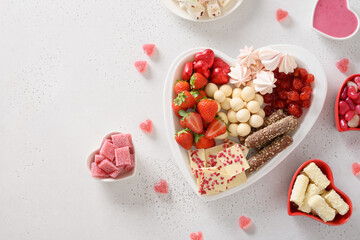 Fototapeta na wymiar Happy Valentines Day. Charcuterie sweet board with different chocolate sweets, strawberries and candies in plate as heart on white background. Top view. Copy space.