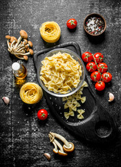 Raw farfalle and tagliatelle paste in a bowl on a cutting Board with mushrooms, tomatoes and spices.